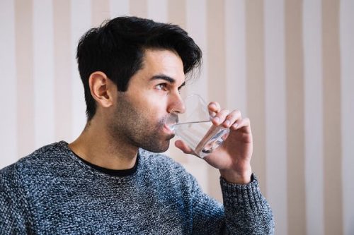  Persona bebiendo agua en vaso de vidrio como hábito de hidratación saludable para prevenir cálculos renales