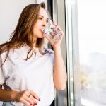 Mujer adulta bebiendo agua filtrada en vaso de cristal en cocina luminosa representando hidratación y salud hormonal