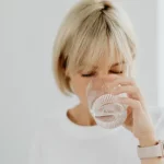 Persona bebiendo agua purificada en casa desde un vaso de cristal
