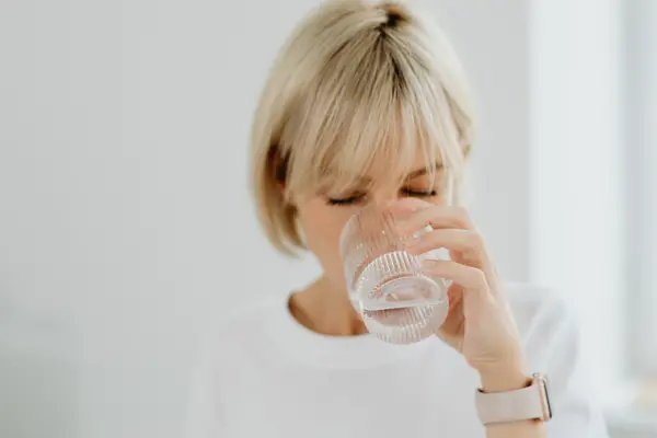 Persona bebiendo agua purificada en casa desde un vaso de cristal